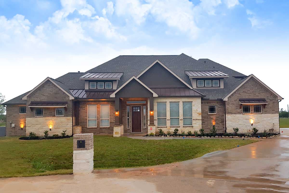 House plan exterior. One-story house with brick and stone facade, gabled roof, and dormers. Features include a covered entry and a driveway.