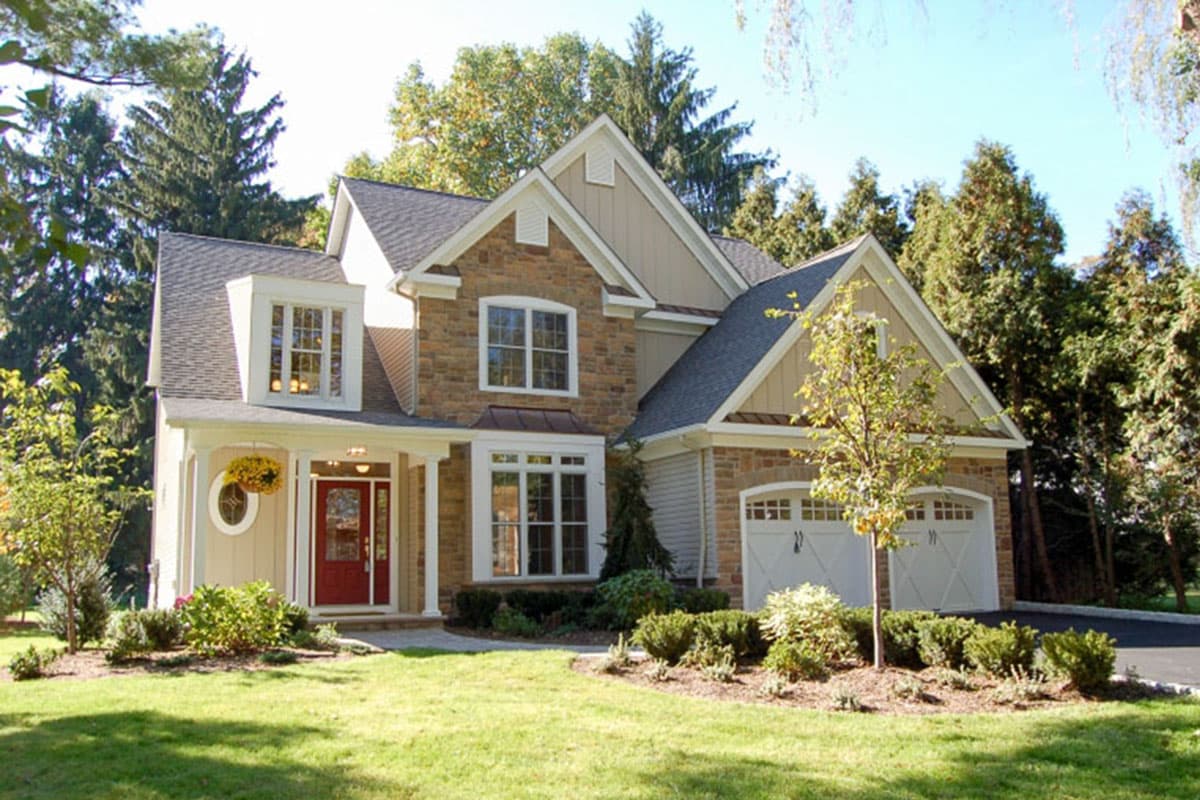 House plan exterior with stone facade, multiple gables, and a front porch. Features include a two-car garage and dormer windows.