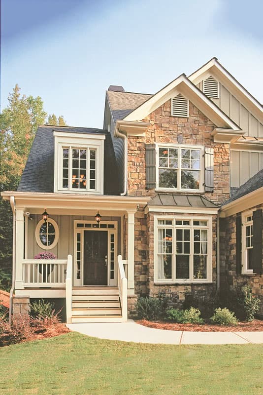 House plan exterior: Two-story home with stone facade, covered porch, dormer window, and gabled rooflines.