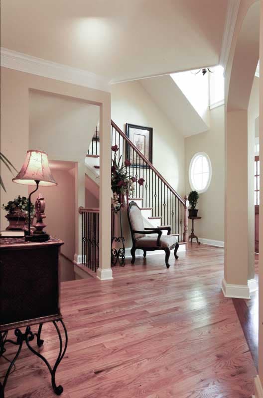 Interior view of a house foyer with a staircase, dark wood banister, oval window, and hardwood floors.