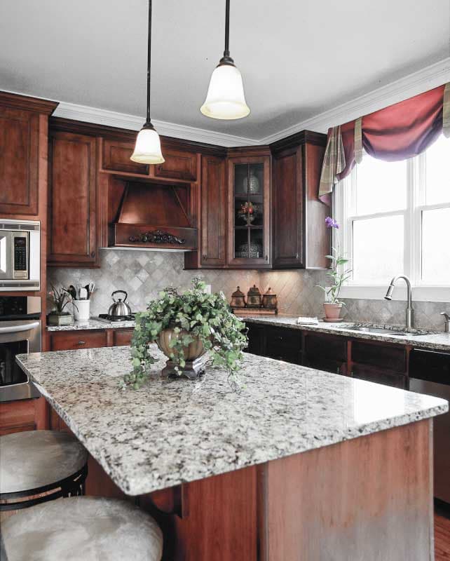 Kitchen interior with granite island, dark wood cabinetry, tile backsplash, stainless steel appliances, and pendant lighting.