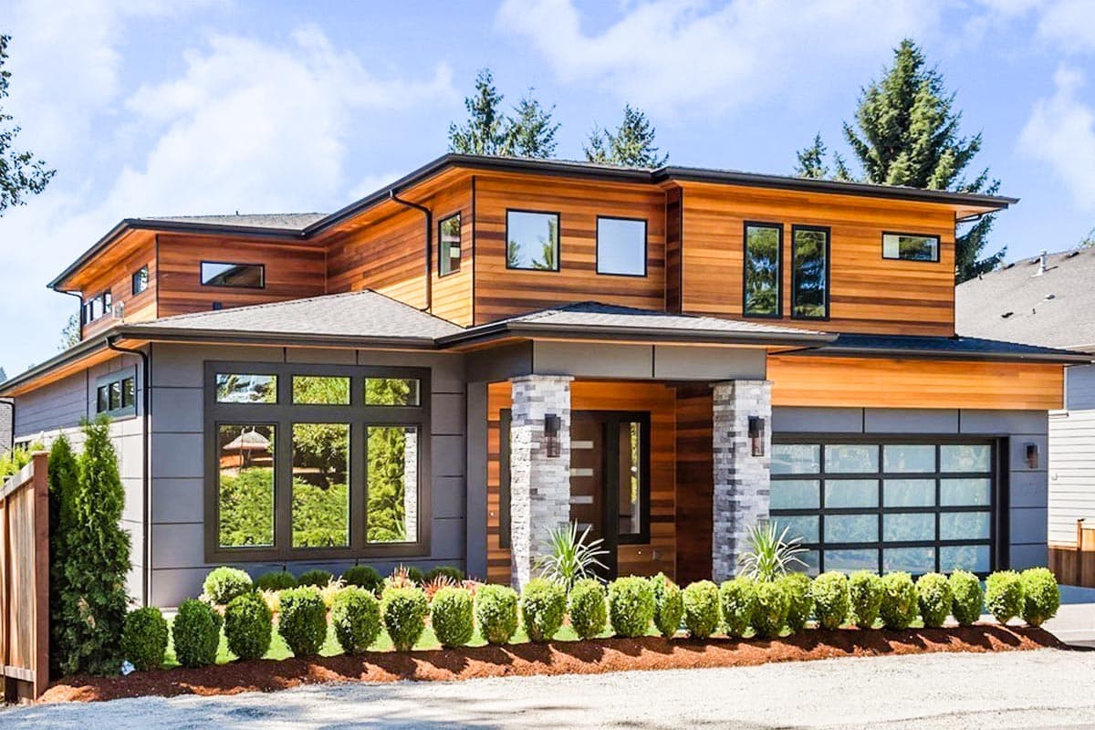 Modern house plan exterior with two stories, wood and gray siding, stone columns, and glass garage door.