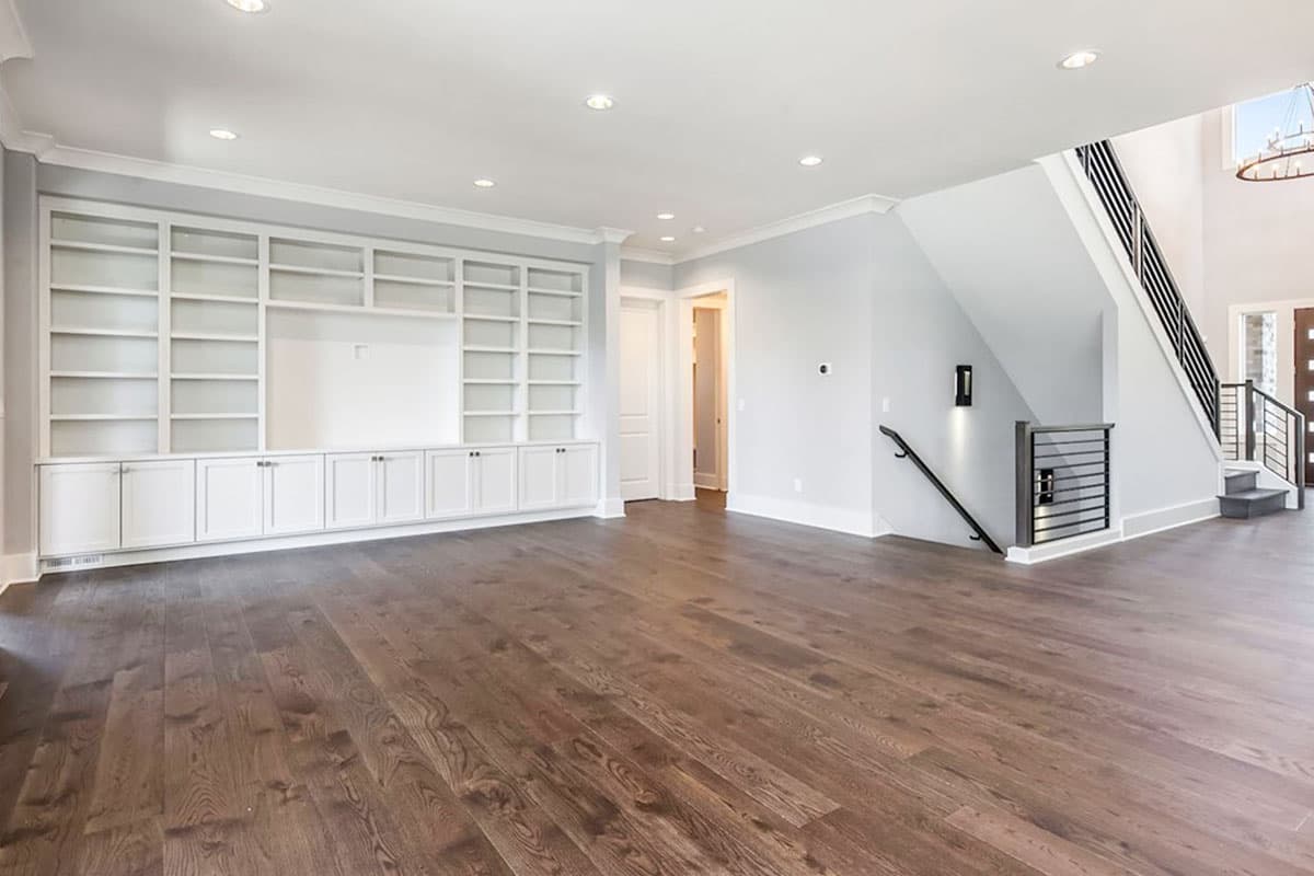 Interior view of a modern home interior with a built-in shelving unit, stairs with metal railings, and hardwood floors.