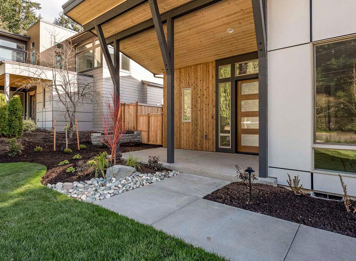 Modern house plan exterior with a wood-clad entrance, wood door with glass panels, and exposed beam overhang.