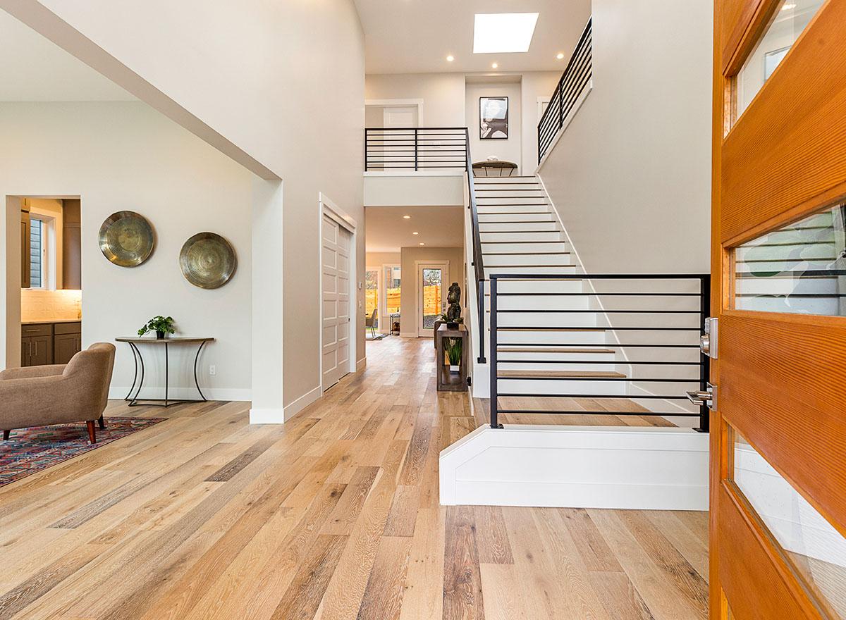 Modern foyer with open staircase, skylight, wood floors, and glass-paneled door.