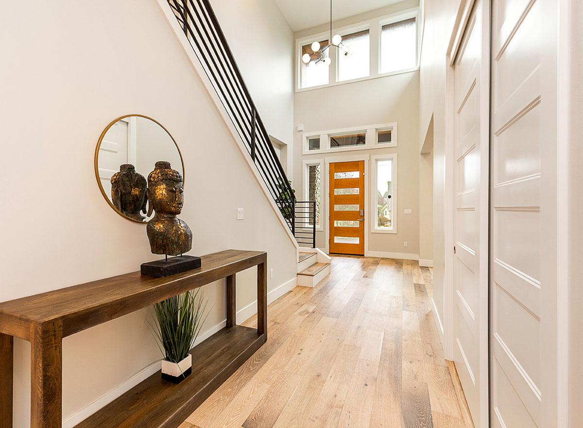 Modern entryway with open staircase, wood plank door, and floor-to-ceiling windows.
