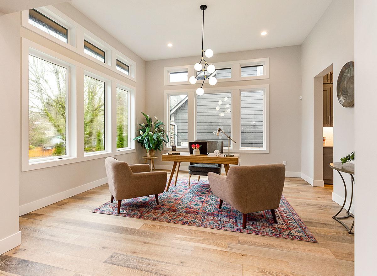 Modern home office with a minimalist desk, two armchairs, and large windows allowing abundant natural light.