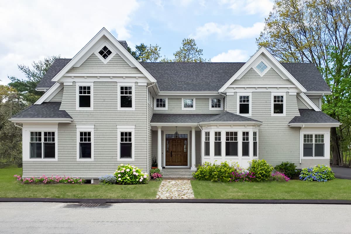 House plan exterior. Two-story, shingle-style home with multiple gables, bay window, and a front porch. Features dormers, and a dark roof.