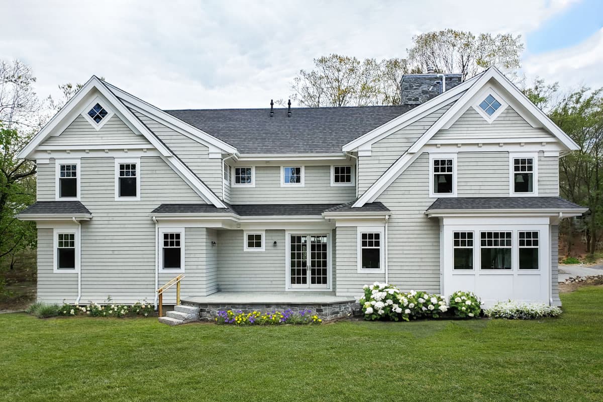 House plan exterior: two-story home with a gray shingle exterior, multiple gables, diamond dormers, and a stone chimney.