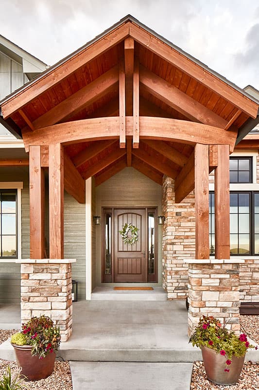 House plan exterior with timber-framed gable entry, stone-clad pillars, and double-door entry.