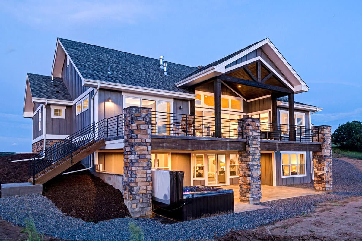 Modern Farmhouse house plan exterior with gabled rooflines, a covered upper deck with stone columns, and a walk-out basement with a hot tub.