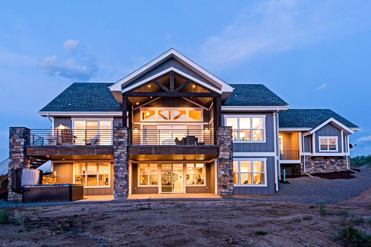 Modern house plan exterior with stone pillars, multiple gables, and a covered upper-level deck with exposed beams.