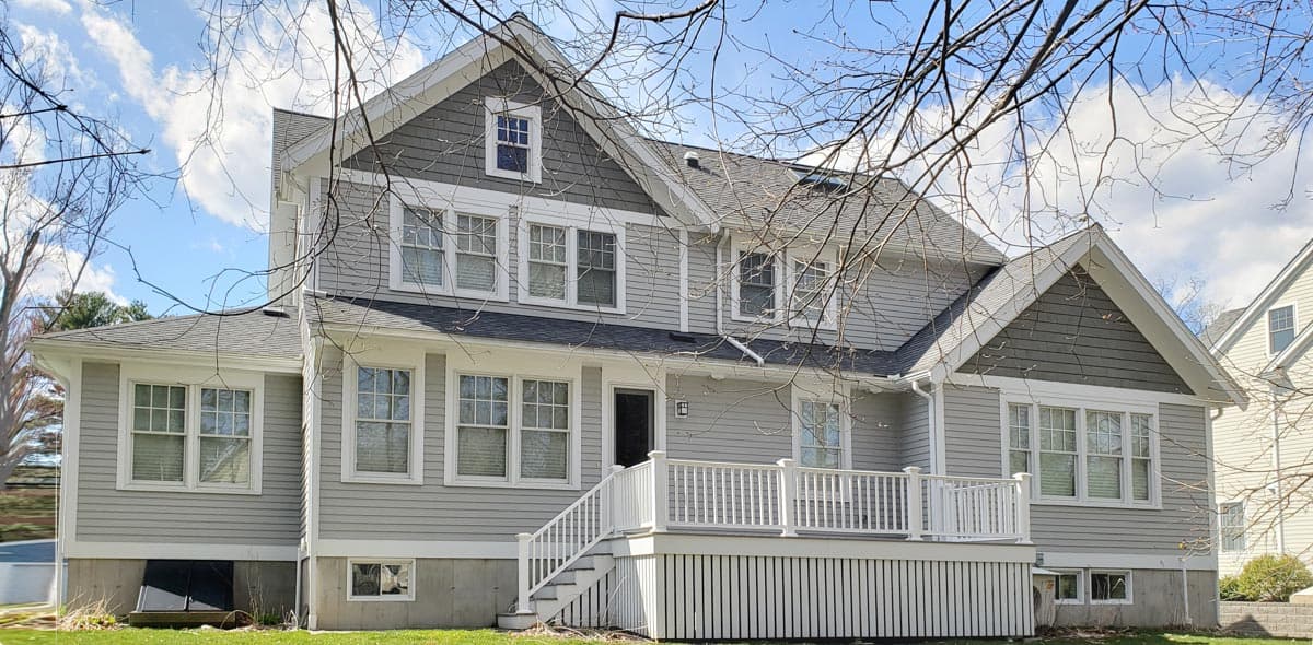 House plan exterior of a multi-story home with a large deck, gables, dormers, and vinyl siding.