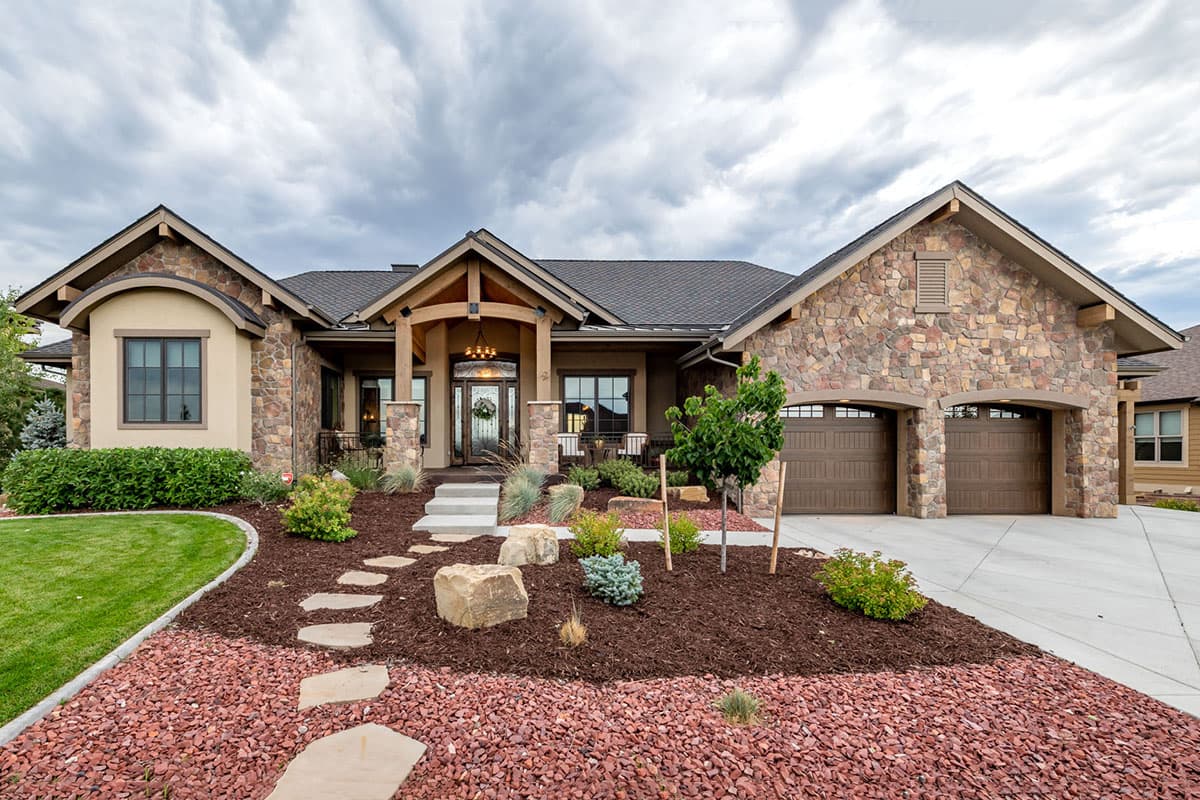 House plan exterior with stone accents, Craftsman-style entrance, and a two-car garage. Features include a gabled roofline and an arched window.