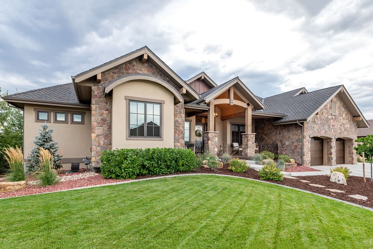 House plan exterior: Ranch style, single-story home with stone accents, arched window, covered entry with timber beams, and a three-car garage.