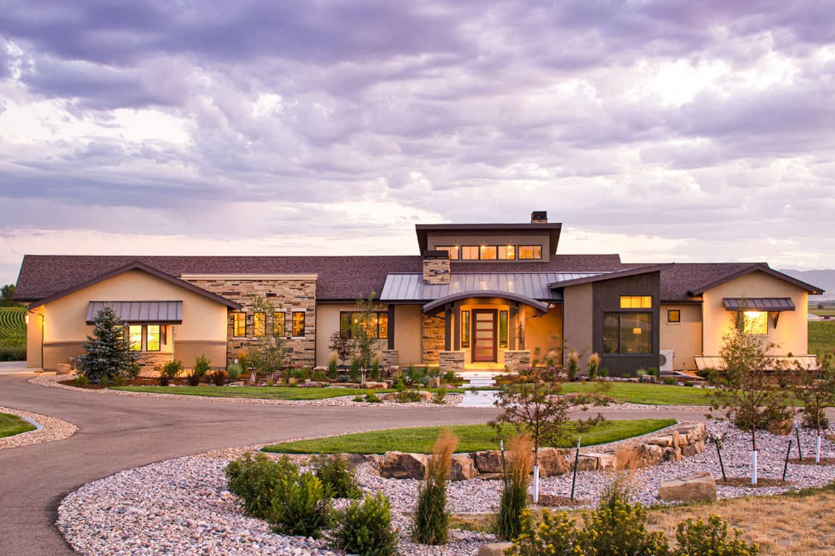 Modern ranch house plan exterior with stone accents, multiple gables, metal roof overhangs, and a covered entry with glass doors.