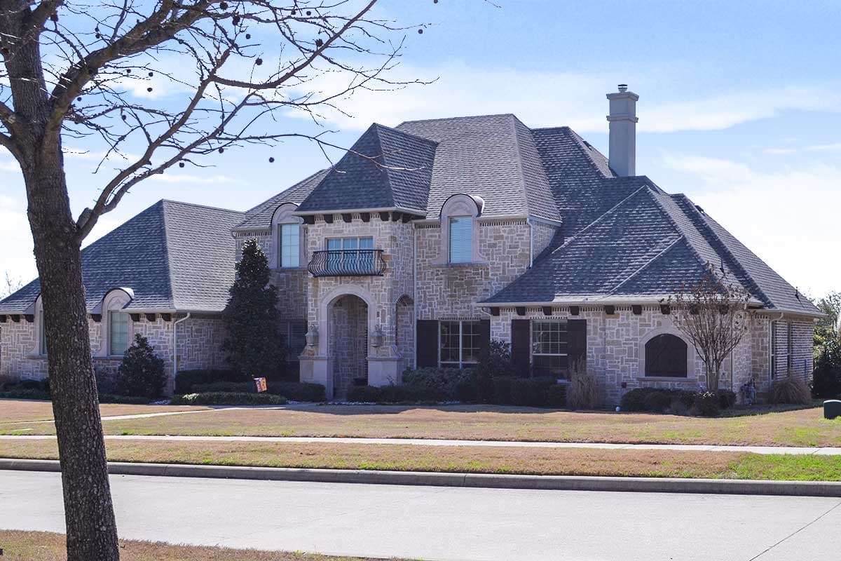 House plan exterior: Two-story stone residence with a complex roofline, arched entryway, Juliette balcony, and prominent chimney.