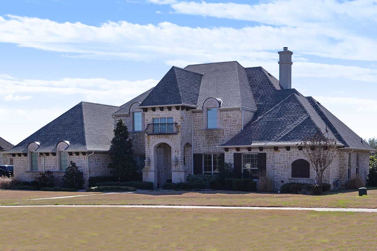 House plan exterior. Two-story, stone facade with multiple gables. Features include arched entry, dormers, and a prominent chimney.