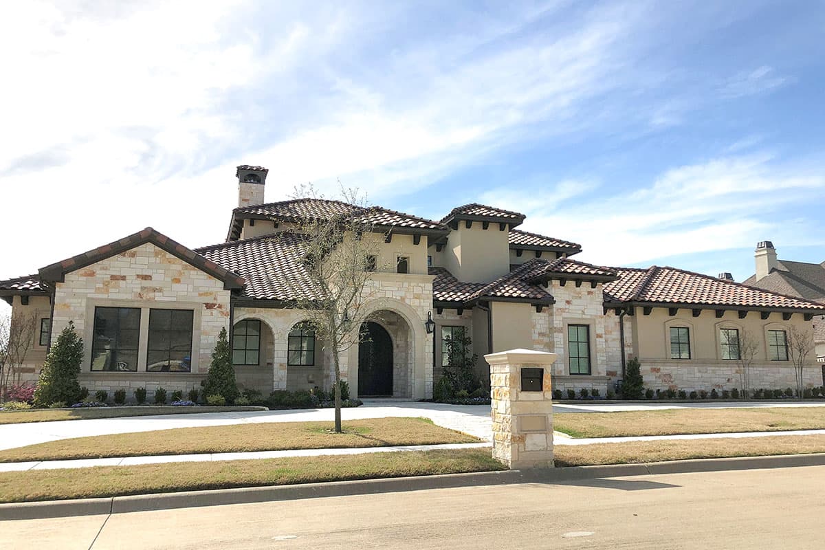 Mediterranean style house plan exterior with stone accents, arched entryway, multiple gables, and tile roof.