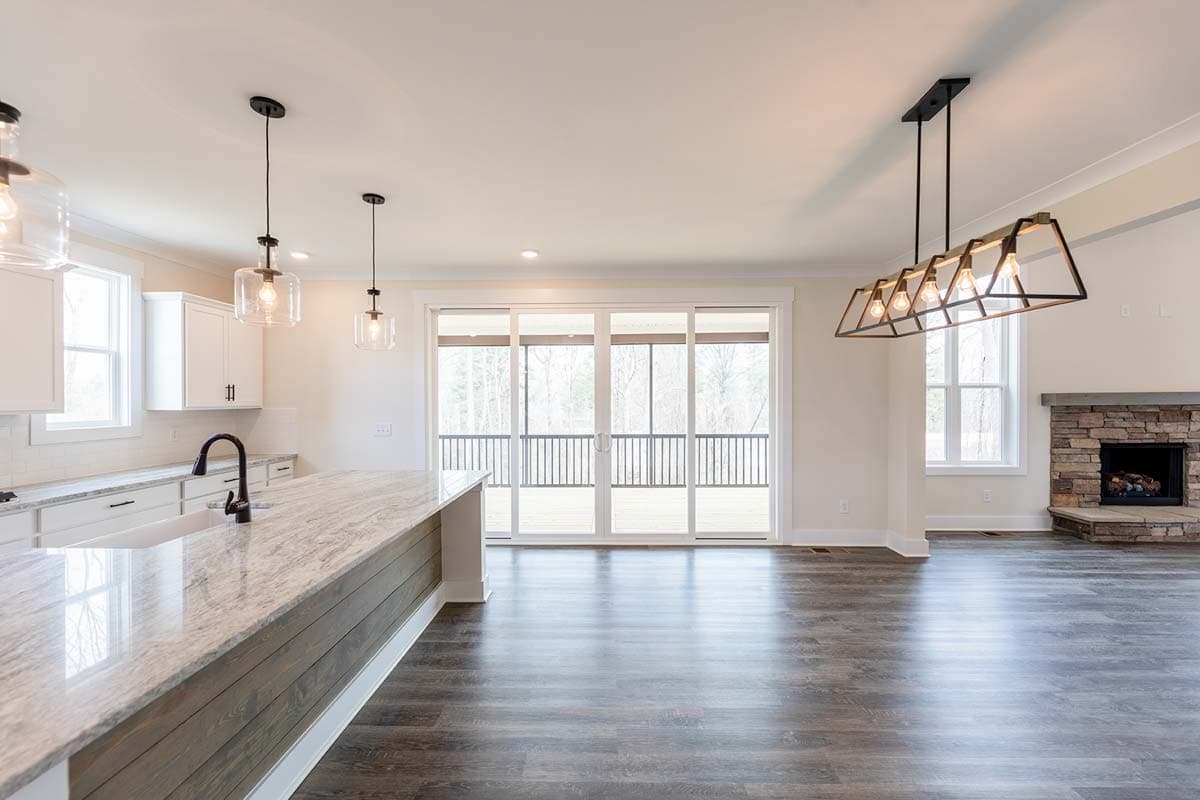 Open concept kitchen and great room with island, stone fireplace, and sliding glass doors to deck.