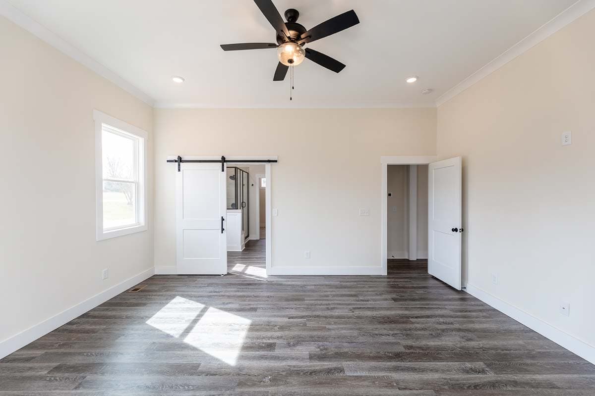 Interior view of a bedroom with a barn door leading to a bathroom, a ceiling fan, and a window. Architectural house plan.