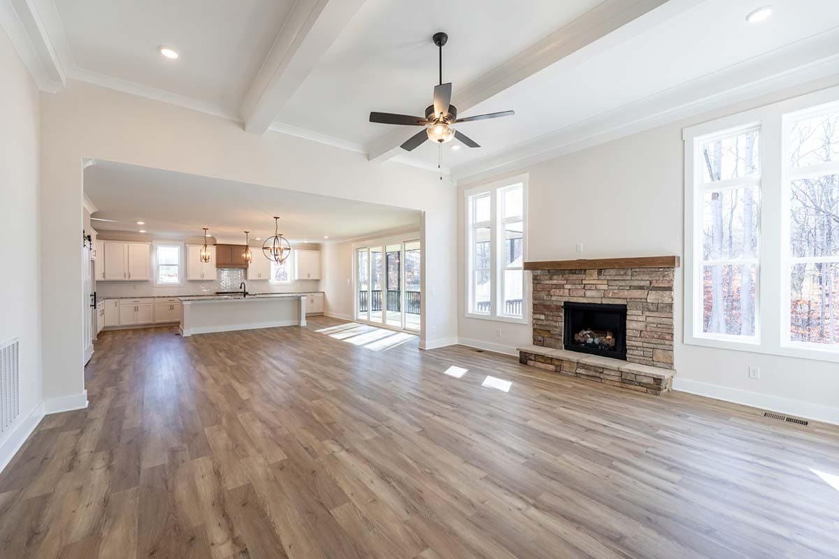 Open concept great room with stone fireplace, vaulted ceiling, and view of kitchen with island.