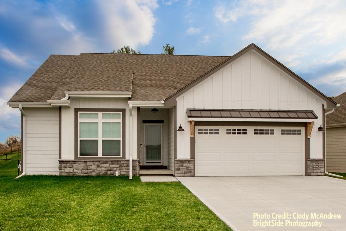 House plan exterior. Modern farmhouse style with gabled roof, stone accents on the facade, and a two-car garage with a decorative awning.