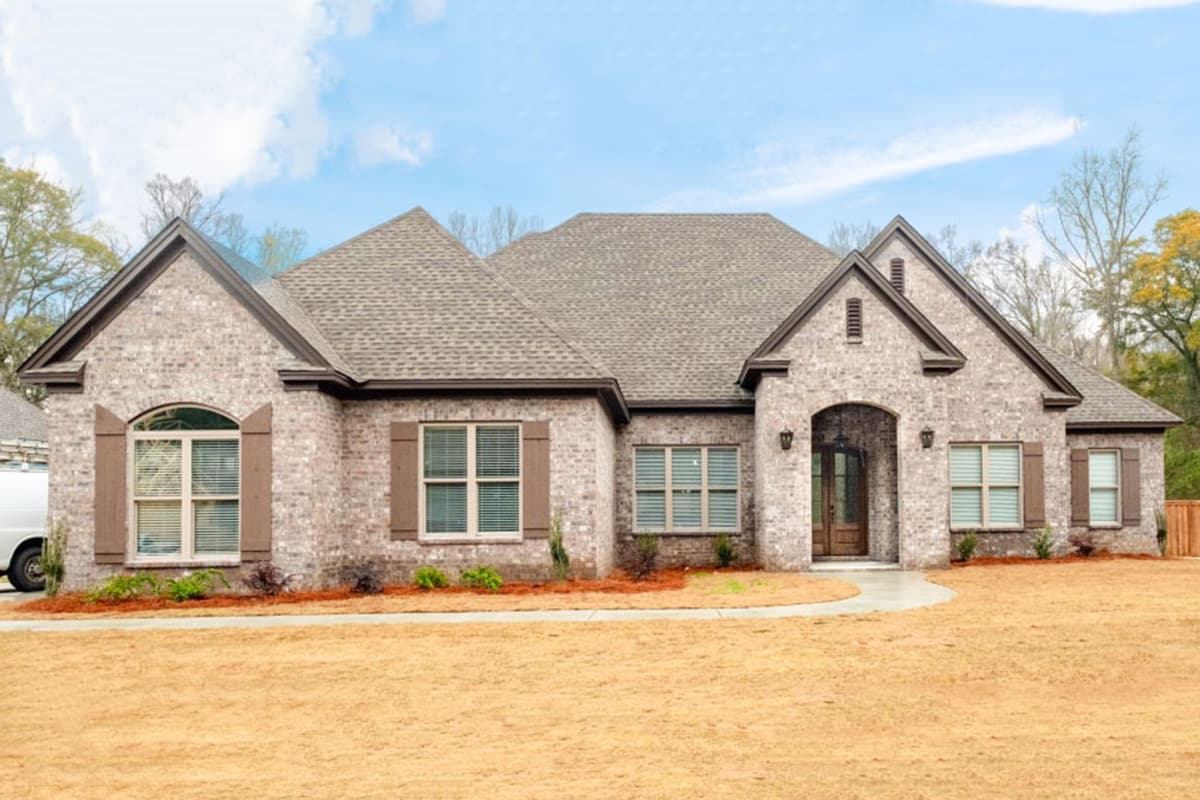 House plan exterior. Single-story, brick facade, gabled roof, arched entry, and decorative shutters are visible.
