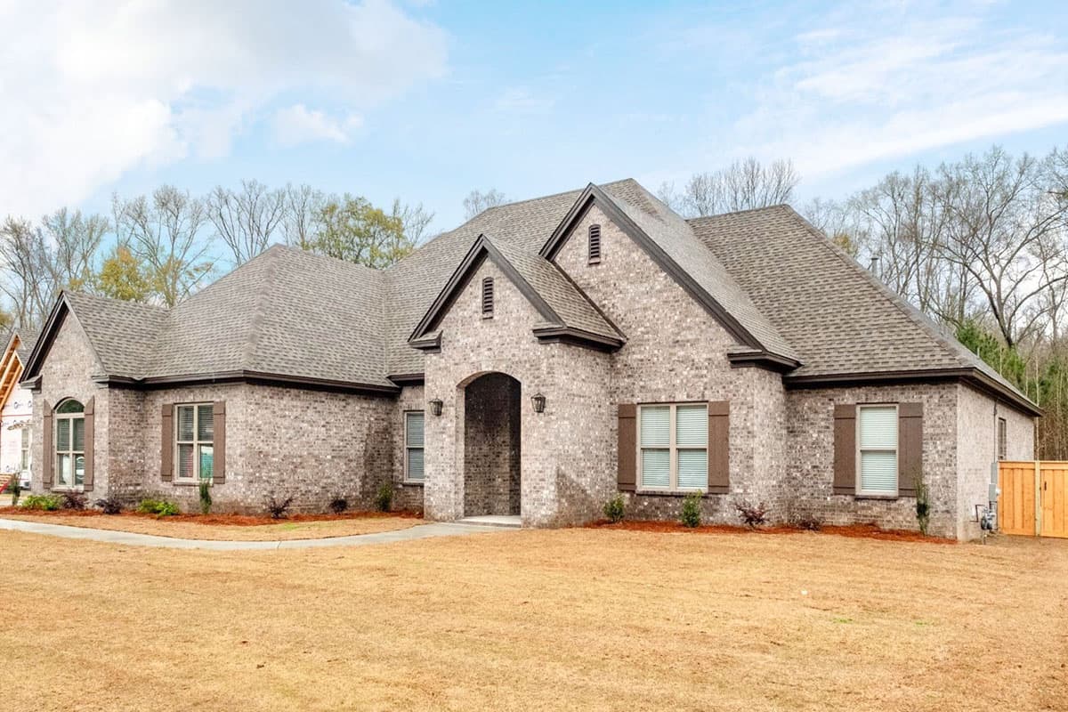 House plan exterior of a one-story brick home with a prominent arched entryway, multiple gables, and brown shutters.