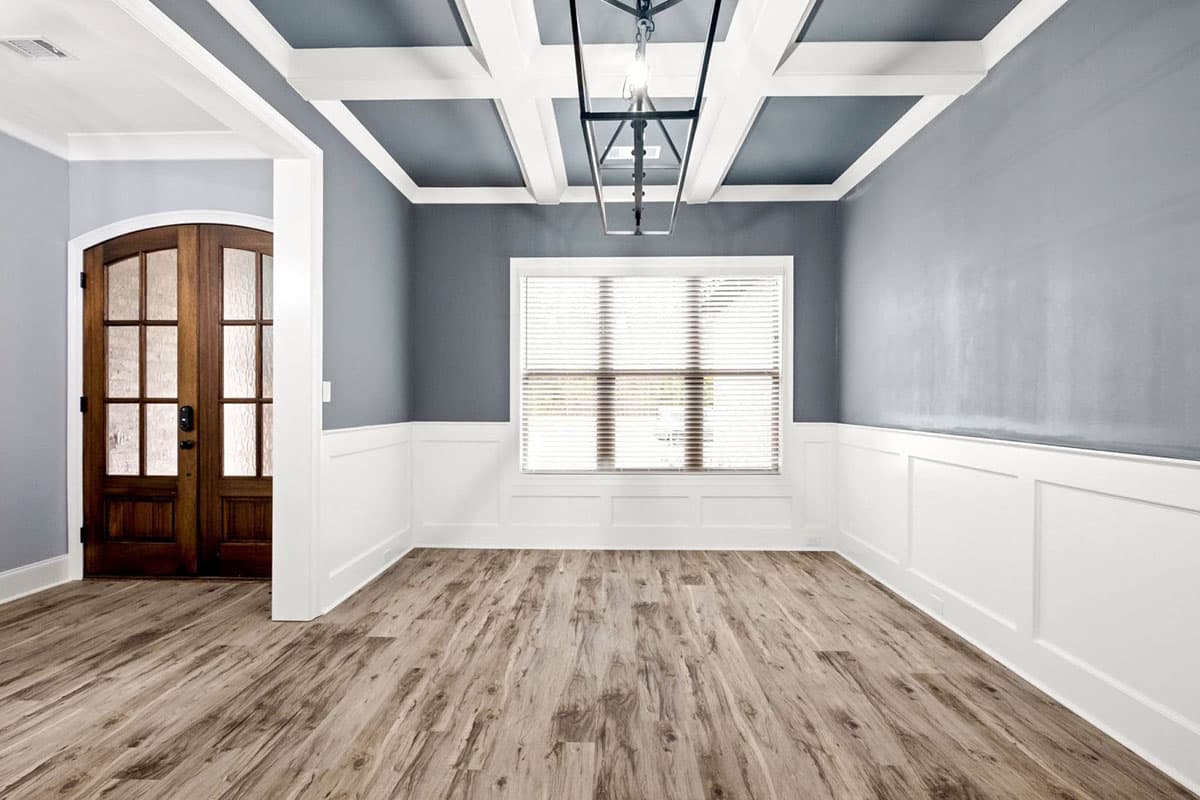 Interior view of dining room with coffered ceiling, double wooden doors, wainscoting, and large window.