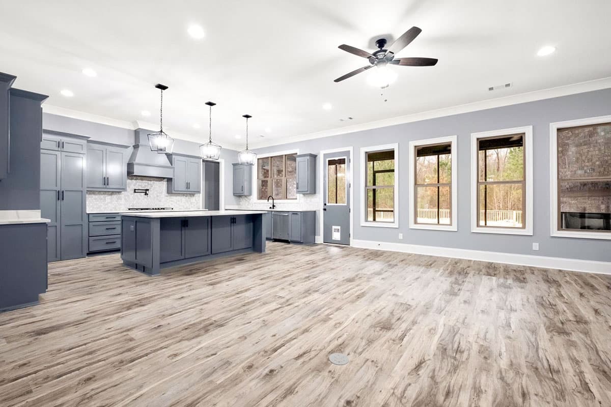 Open-concept kitchen with a large island, gray cabinetry, white countertops, and a view of the dining area with windows.