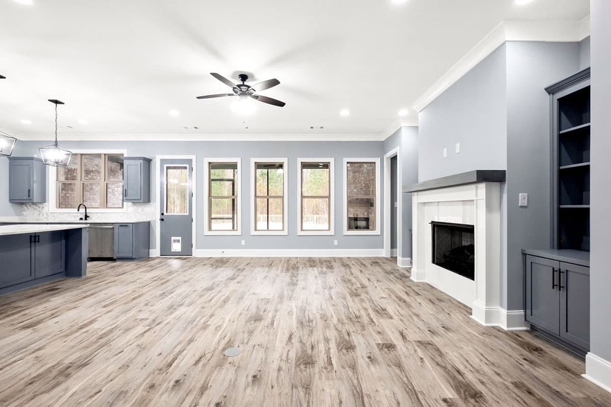 Open-concept living area with kitchen, fireplace, ceiling fan, and large windows.