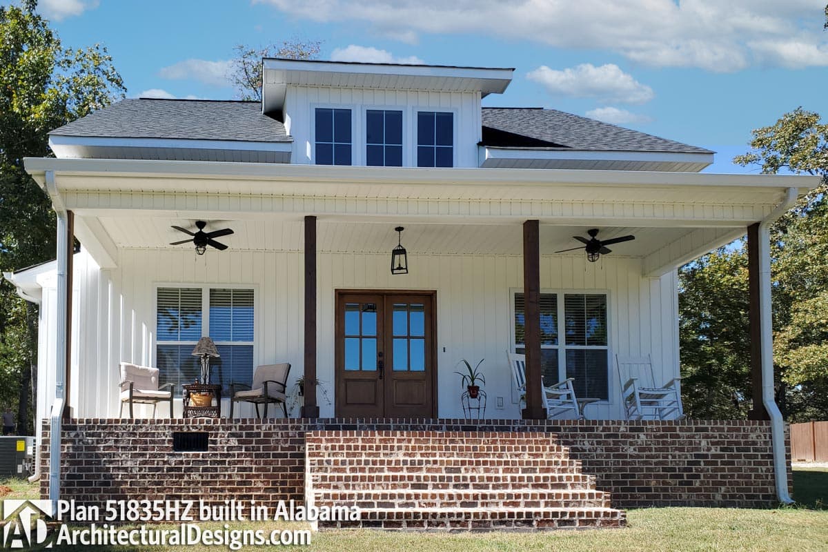 House plan exterior: Modern Farmhouse style, two stories, wide covered porch with wood columns, dormer with three windows, brick foundation.