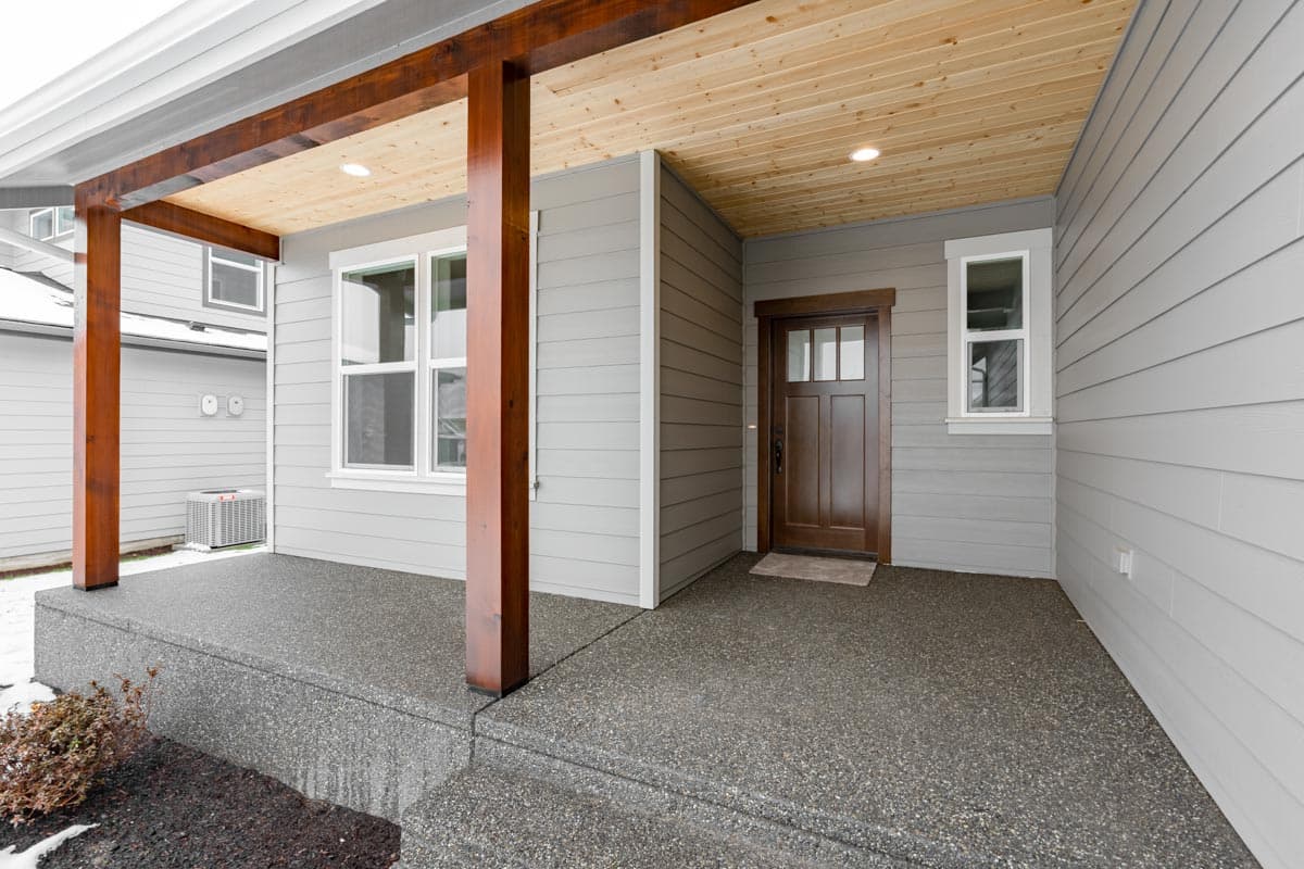 House plan exterior: Covered porch with wood beams, concrete floor, and wood front door with transom.