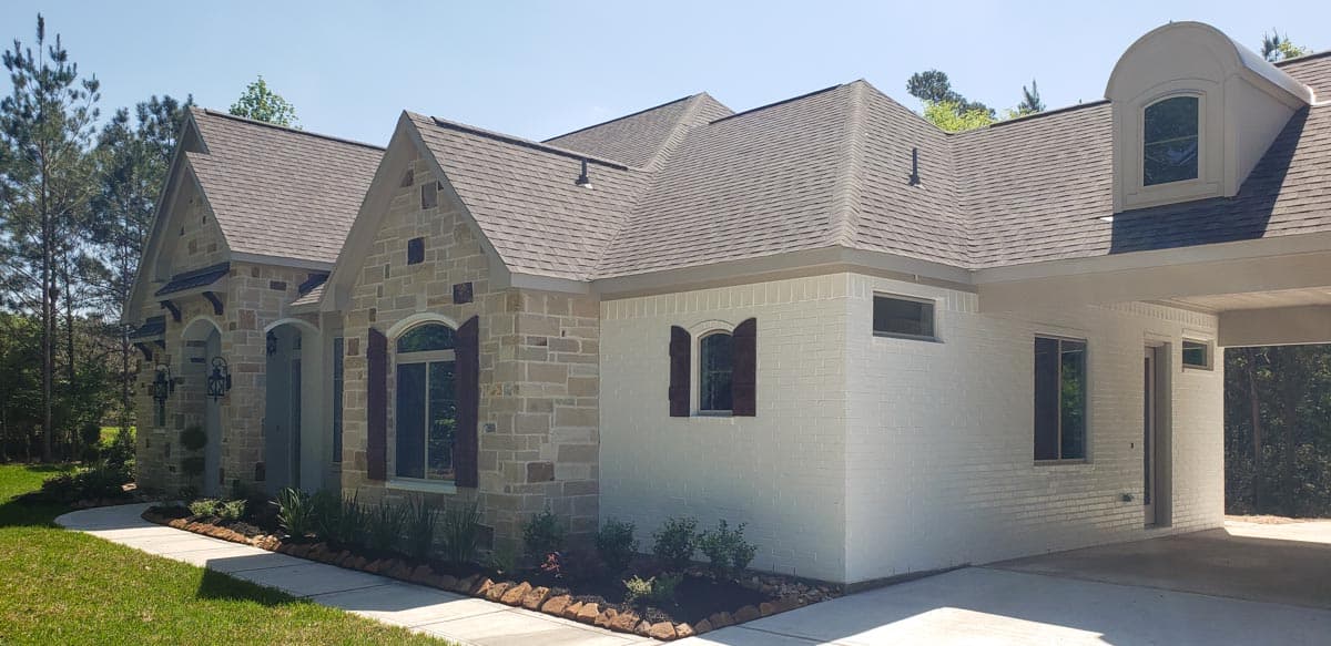 House plan exterior shows stone and white brick facade, multiple gables, arched entryways, and a covered carport.