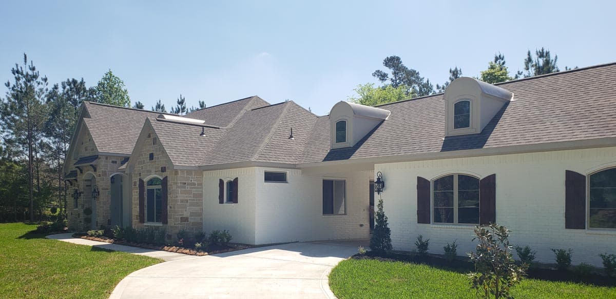 House plan exterior: One-story French Country style with stone accents, a gabled entrance, arched windows, and dormers.