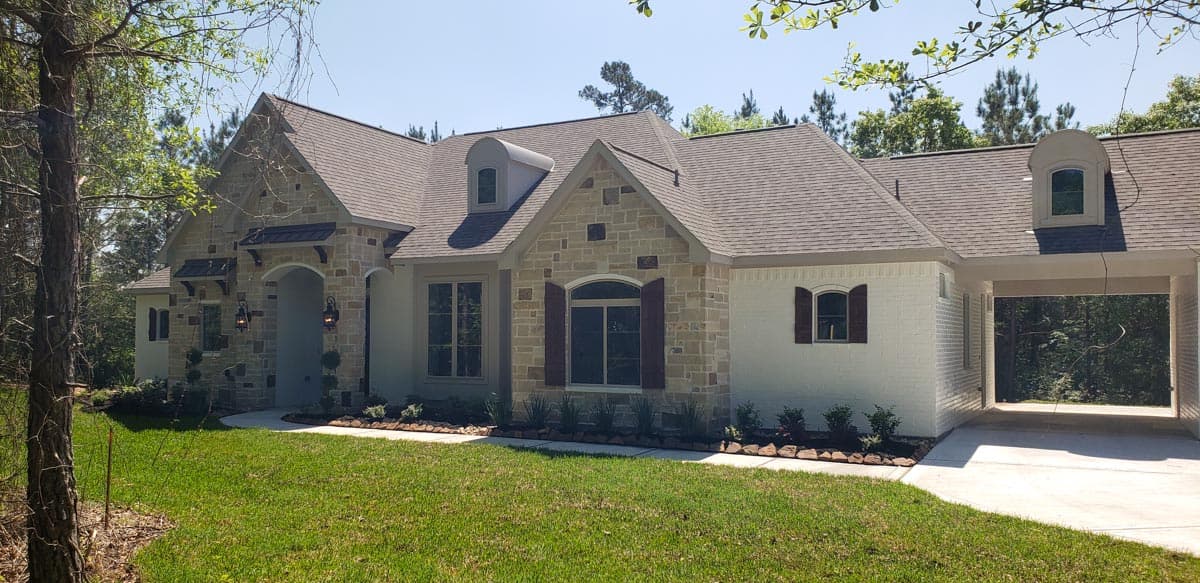 House plan exterior with stone and painted brick facade. Features include dormers, a covered entryway, and an attached garage. Two story. 