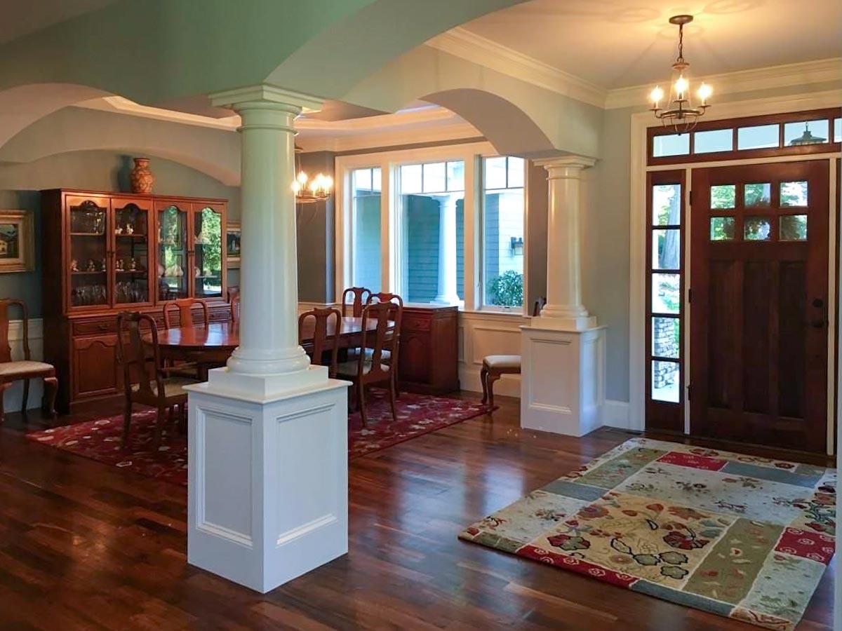 Interior view of a dining room and entryway featuring columns, a wooden china cabinet, dining set, and a paneled front door.