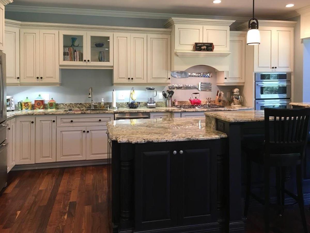 Kitchen interior with cream cabinetry, granite countertops, dark island with seating, and stainless steel double ovens.