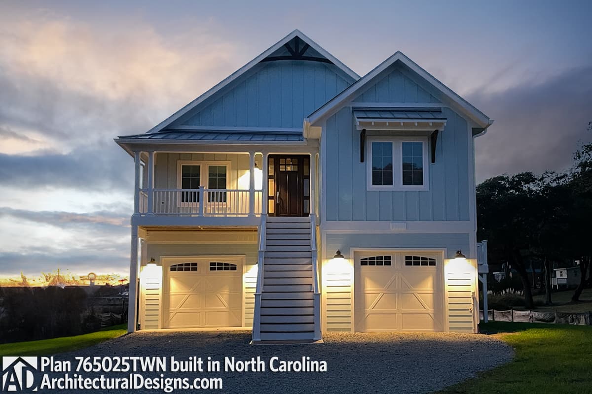 House plan exterior: Two-story coastal style with wraparound balcony, steep gable roof, and two-car garage.