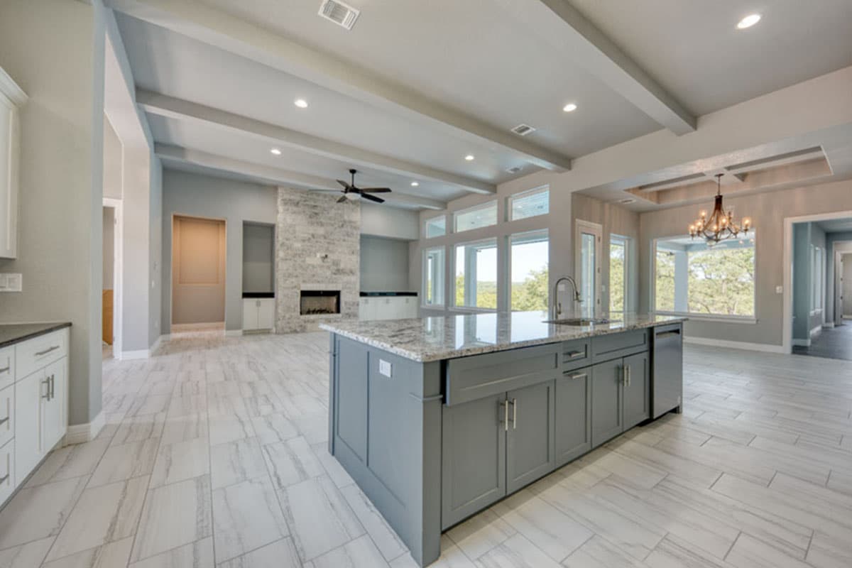 Open concept living area with gray island, stone fireplace, and large windows with natural views.