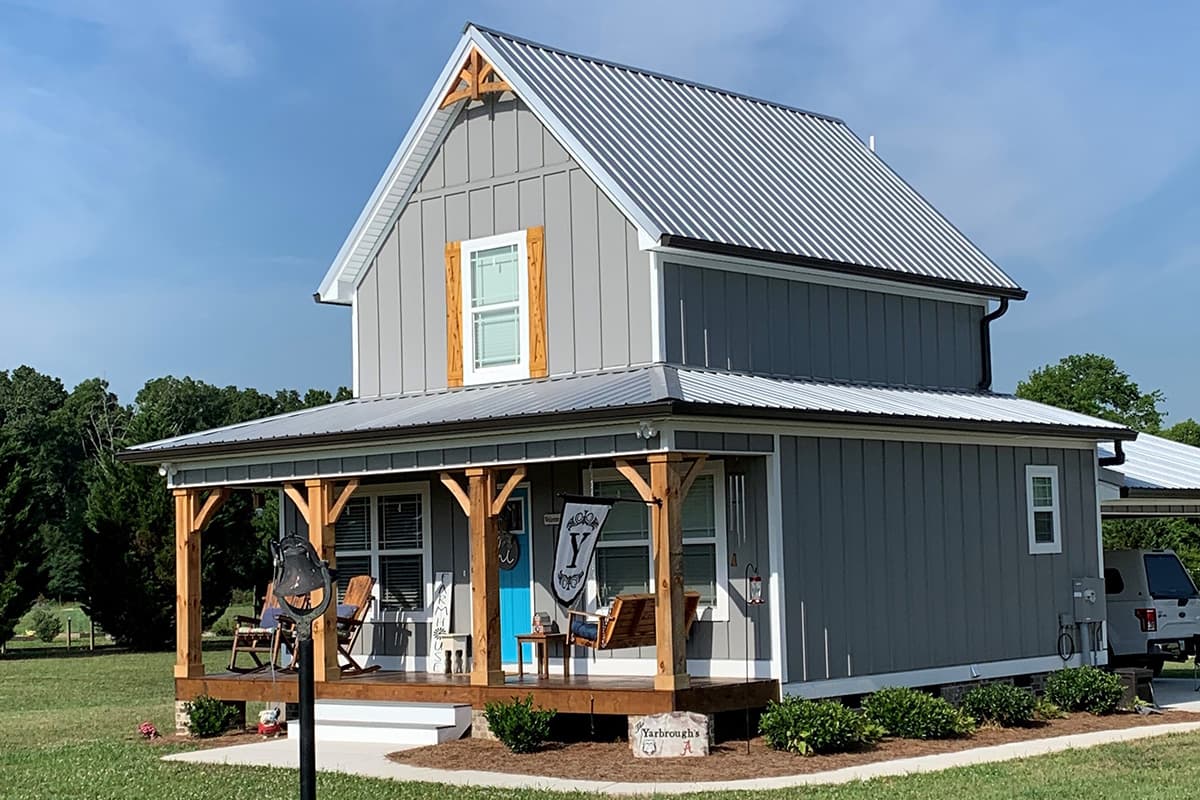House plan exterior view, two-story farmhouse with a metal roof, front porch with exposed wooden supports, and board-and-batten siding.