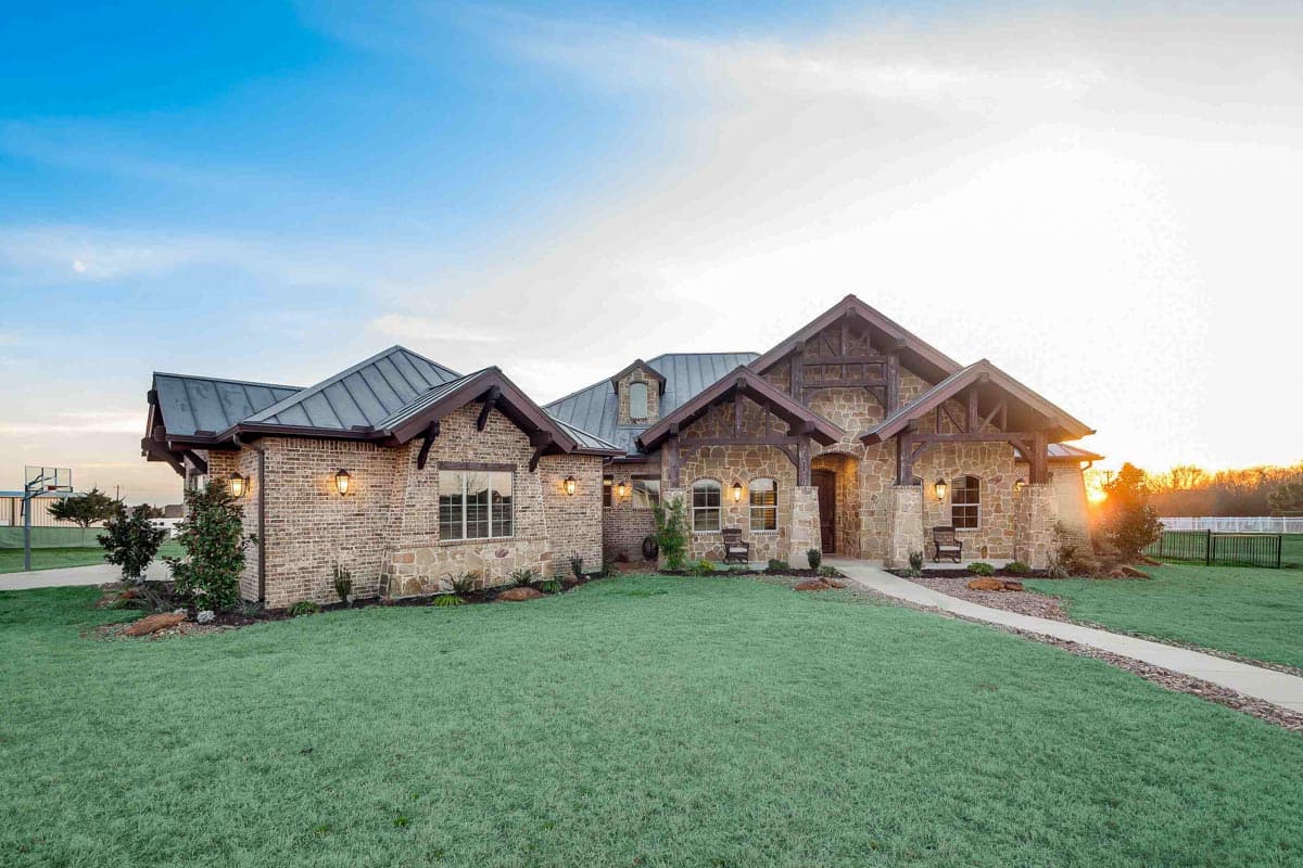 House plan exterior with stone and brick facade, multiple gables, dark metal roof, and exposed wood beams.