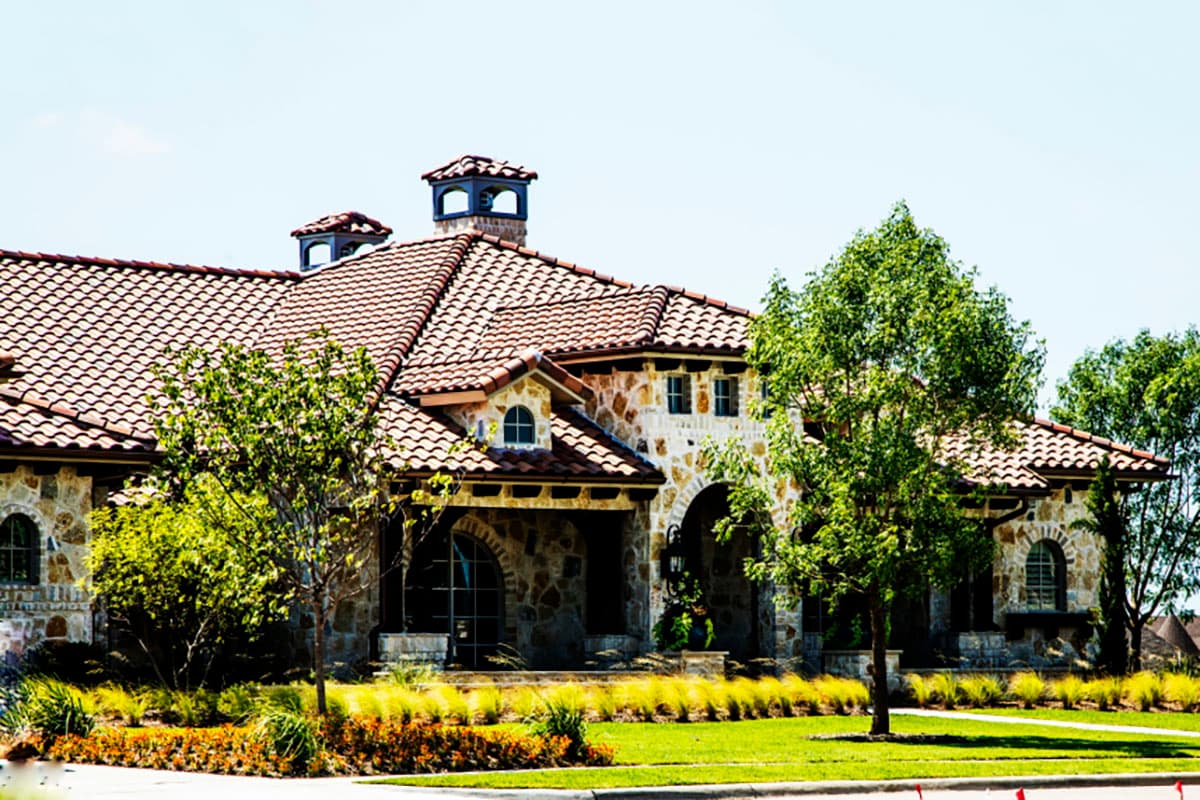 House plan exterior: Mediterranean style, two stories, red tile roof, stone facade, arched entryway, and decorative chimneys.