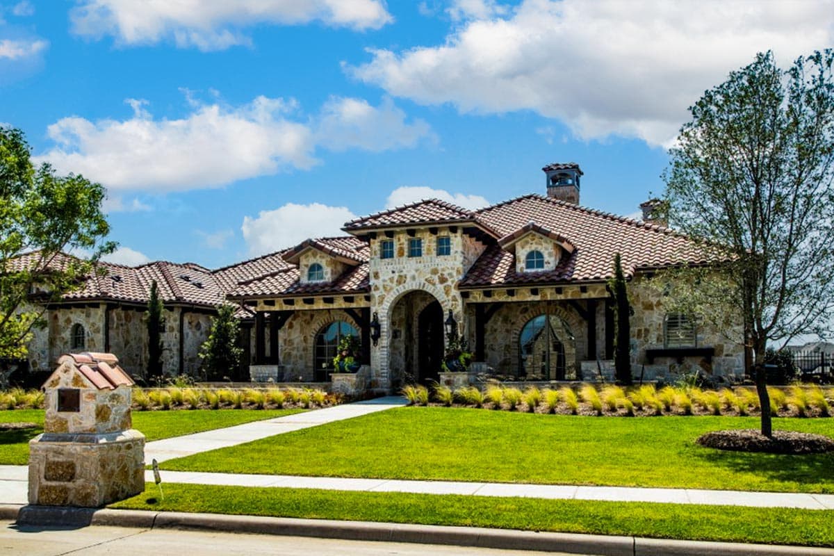 House plan exterior with two stories, stone facade, barrel tile roof, arched entryway, and multiple dormers.