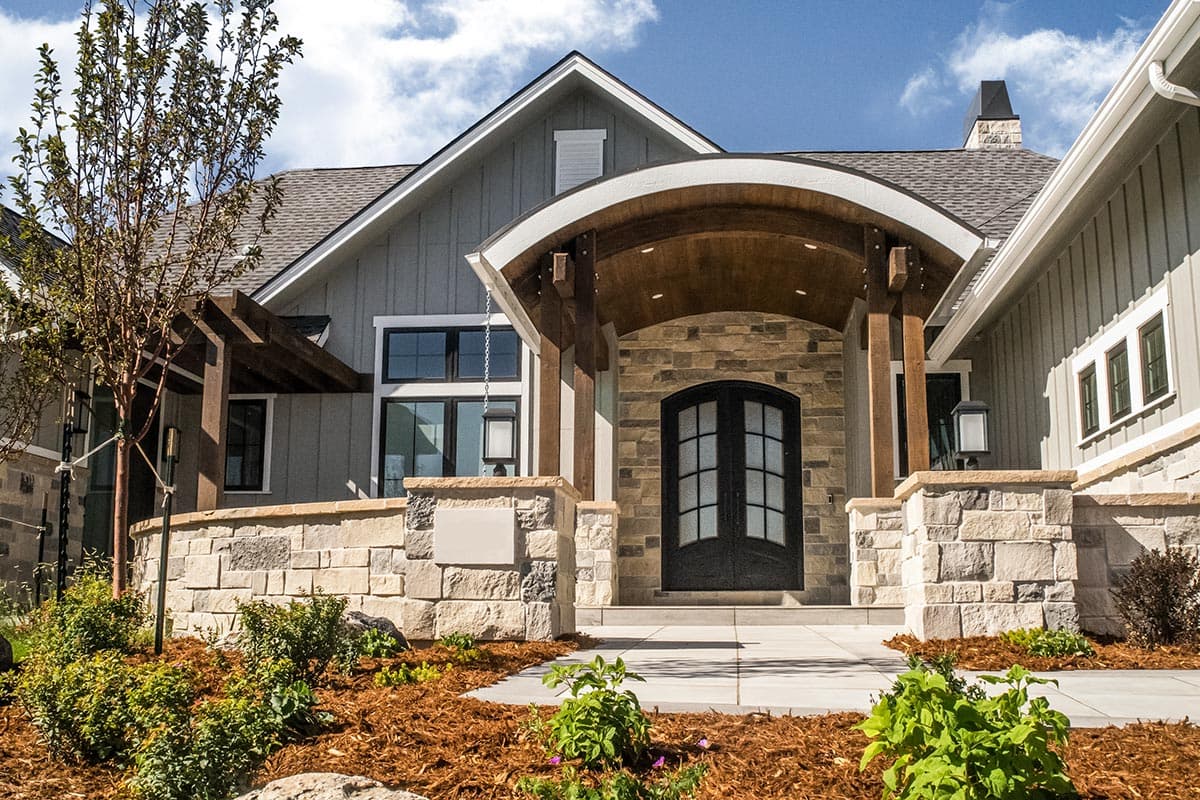 Modern Farmhouse exterior with stone accents, arched entryway with wood beams, board and batten siding, and multiple gables.