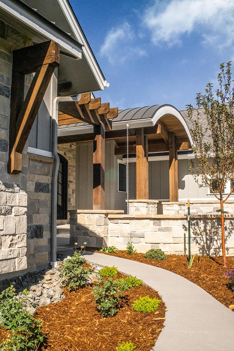House plan exterior with stone accents, wooden pergola, and curved metal roof.