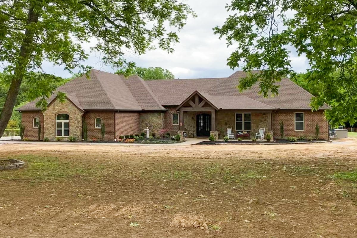 House plan exterior: One-story brick and stone home with a covered entry, gables, and multiple rooflines.