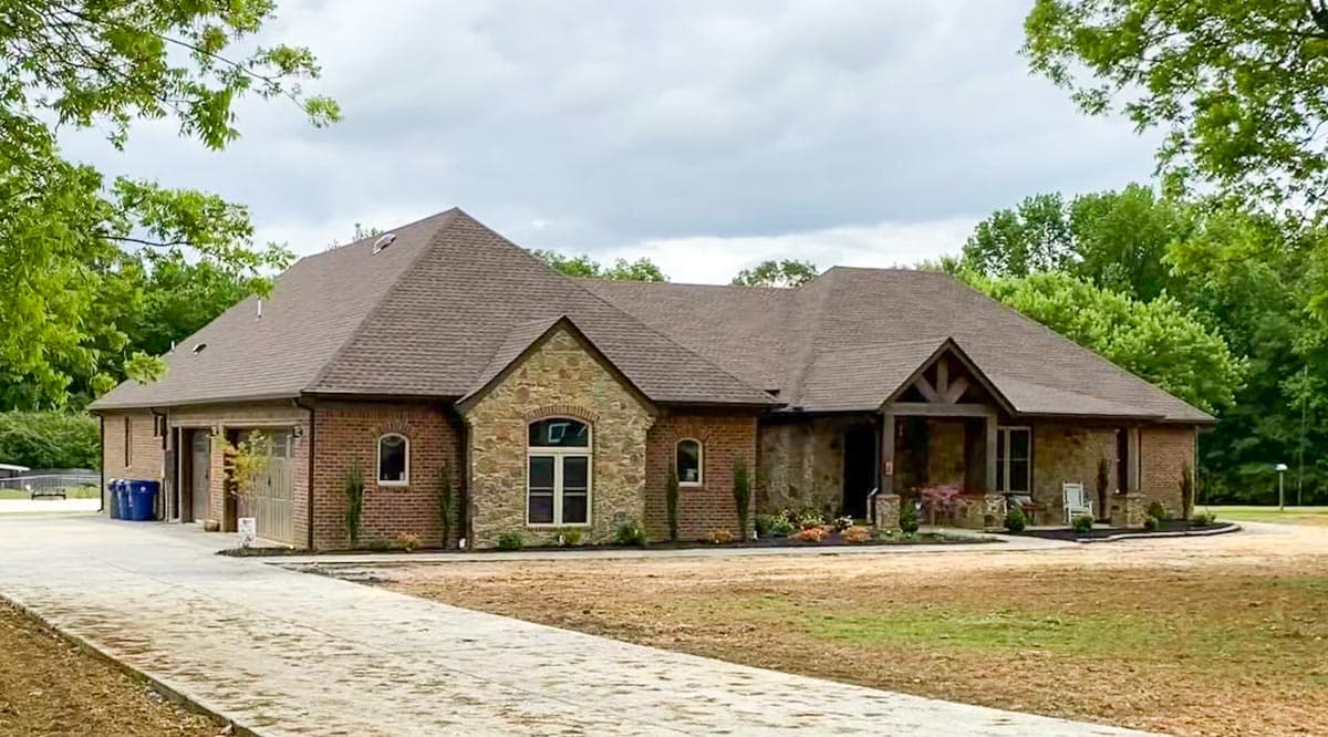 House plan exterior: one-story brick and stone house with gabled roof, covered porch, and attached garage.
