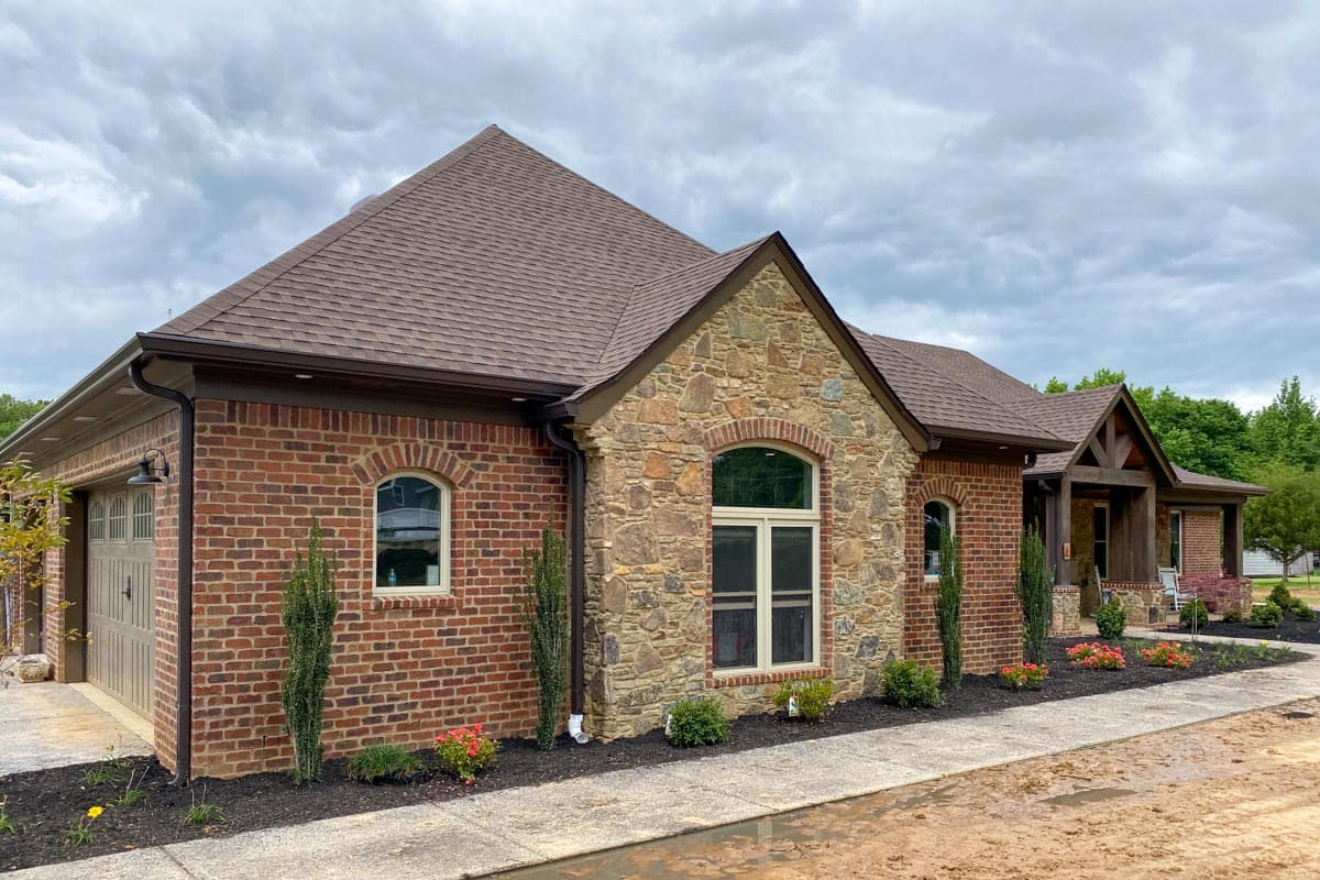 House plan exterior with brick and stone facade, arched windows, and a covered front porch.
